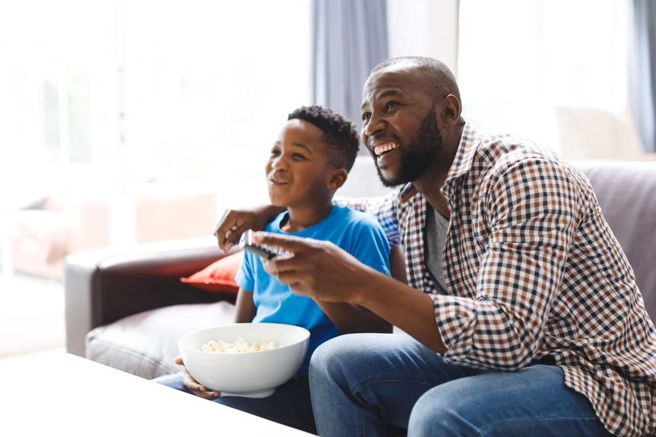 happy-african-american-father-and-son-sitting-on-sofa-watching-tv.jpg